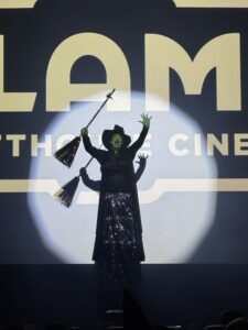 Kitana Sanchez as Elphaba from Wicked performing at the Alamo Drafthouse Cinema screen.