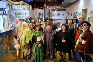 Group in fantasy and Renaissance costumes with rainbow Pride flags at Lazy Beach Brewing for the medieval bar crawl.
