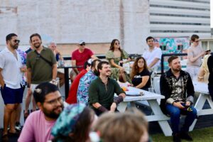 Smiling attendees gather at picnic tables for the Quest for Pride medieval fantasy bar crawl outdoor event.