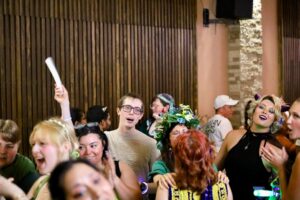 Joyful crowd dancing and cheering at the Quest for Pride medieval fantasy bar crawl, some wearing floral crowns.