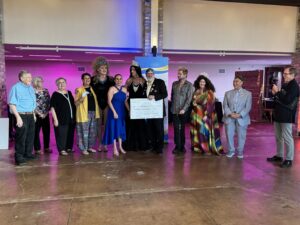 Group at Pride Gala 2025, including drag performers in crowns, holding a large donation check.