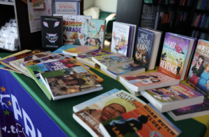 Display table of LGBTQ+ books including The Rainbow Parade, Every Day, and These Vengeful Gods.