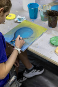 Young artist paints a blue and yellow canvas at an Art Lab for Teens workshop.