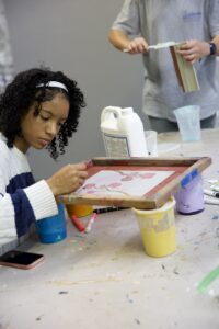 Teen focused on screen printing a floral design at a hands-on art lab workshop.