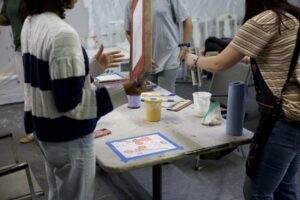 Teens gather around a paint-splattered table making screen-printed and painted artwork at an art lab workshop.
