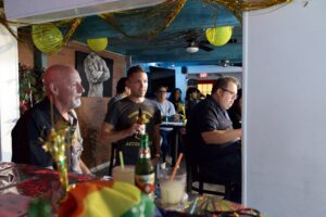 Attendees gather at a festive bar decorated with gold tinsel and balloons during a Pride community event.