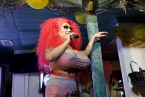 Brigitte Bandit sings into a microphone at a festive Pride event.