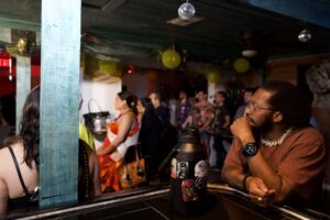 A man rests his chin on his hand, watching attentively at The Loft, upstairs at The Hidden Door, gathering with disco balls and crowd.